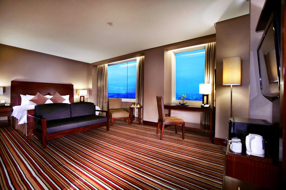 A hotel room with a bed, a sofa, a desk with a lamp, a chair, and a view of the ocean.
