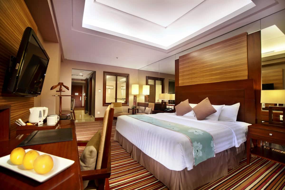 A hotel room with a large bed, a desk with a coffee maker, a TV, and a dining area with a table and chairs.