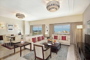 Salón de hotel con sofá, mesa de comedor, candelabro y grandes ventanales con vistas.
