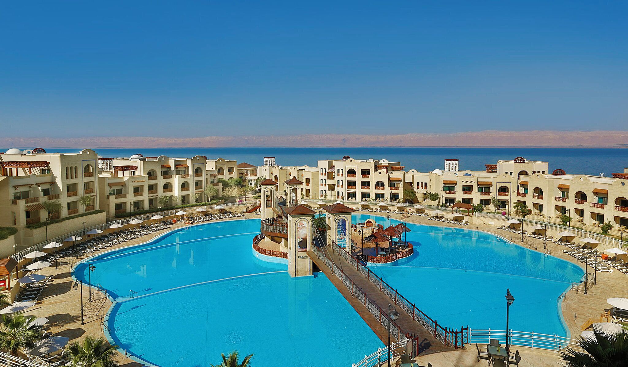 A resort with a large central pool, multiple balconies, and a view of the sea.