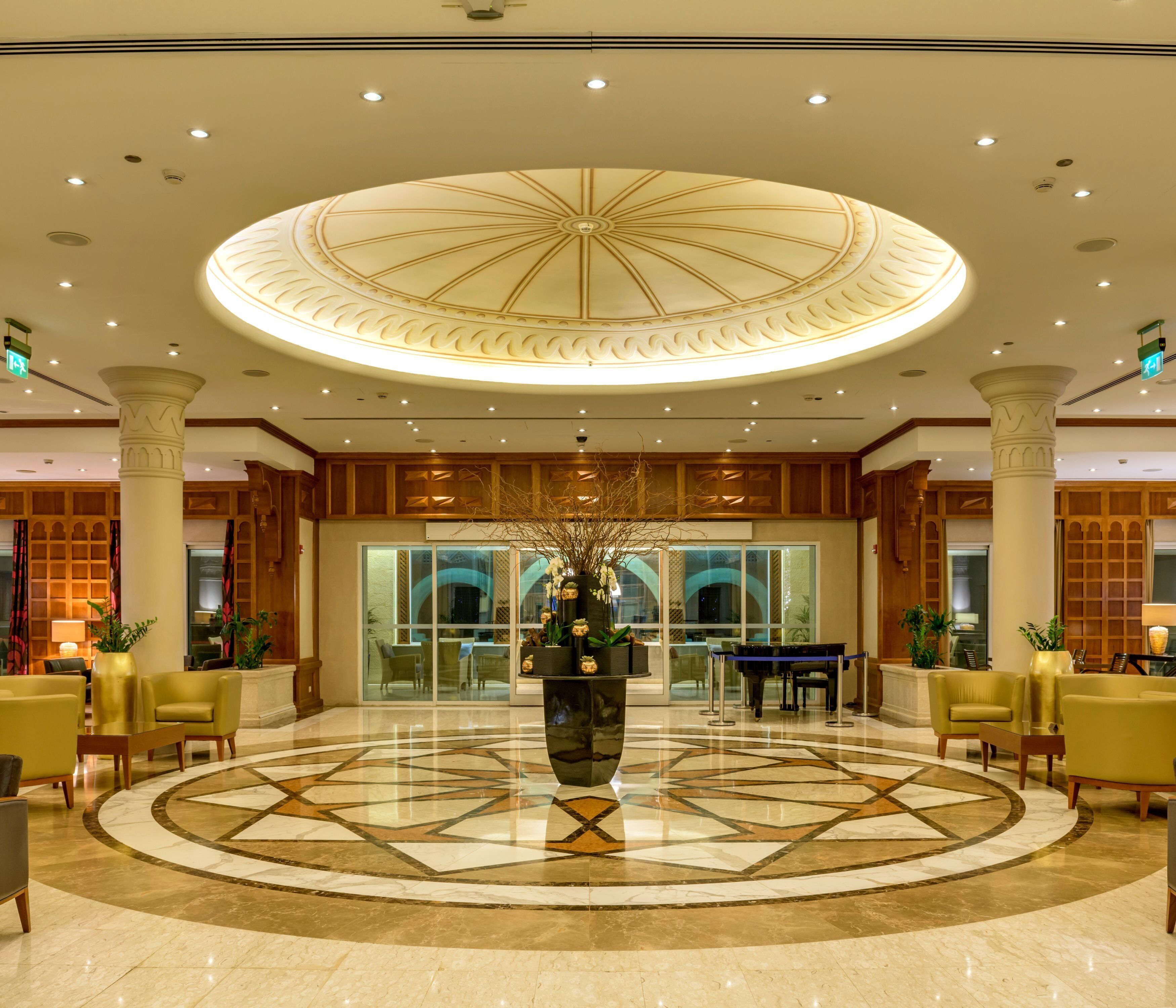 A lobby with a central fountain, marble flooring, and a circular ceiling design.
