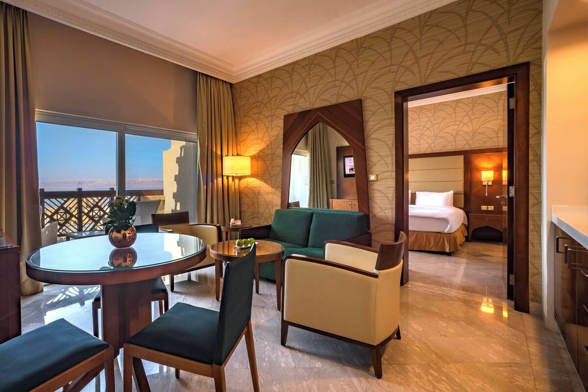 A hotel room with a balcony, a dining area with a round table, a sofa, and a bed.
