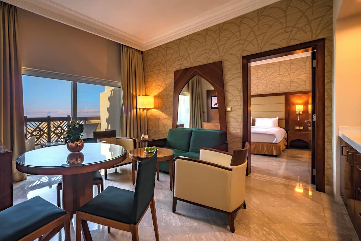 A hotel room with a balcony, a dining area with a round table, a sofa, and a bed.