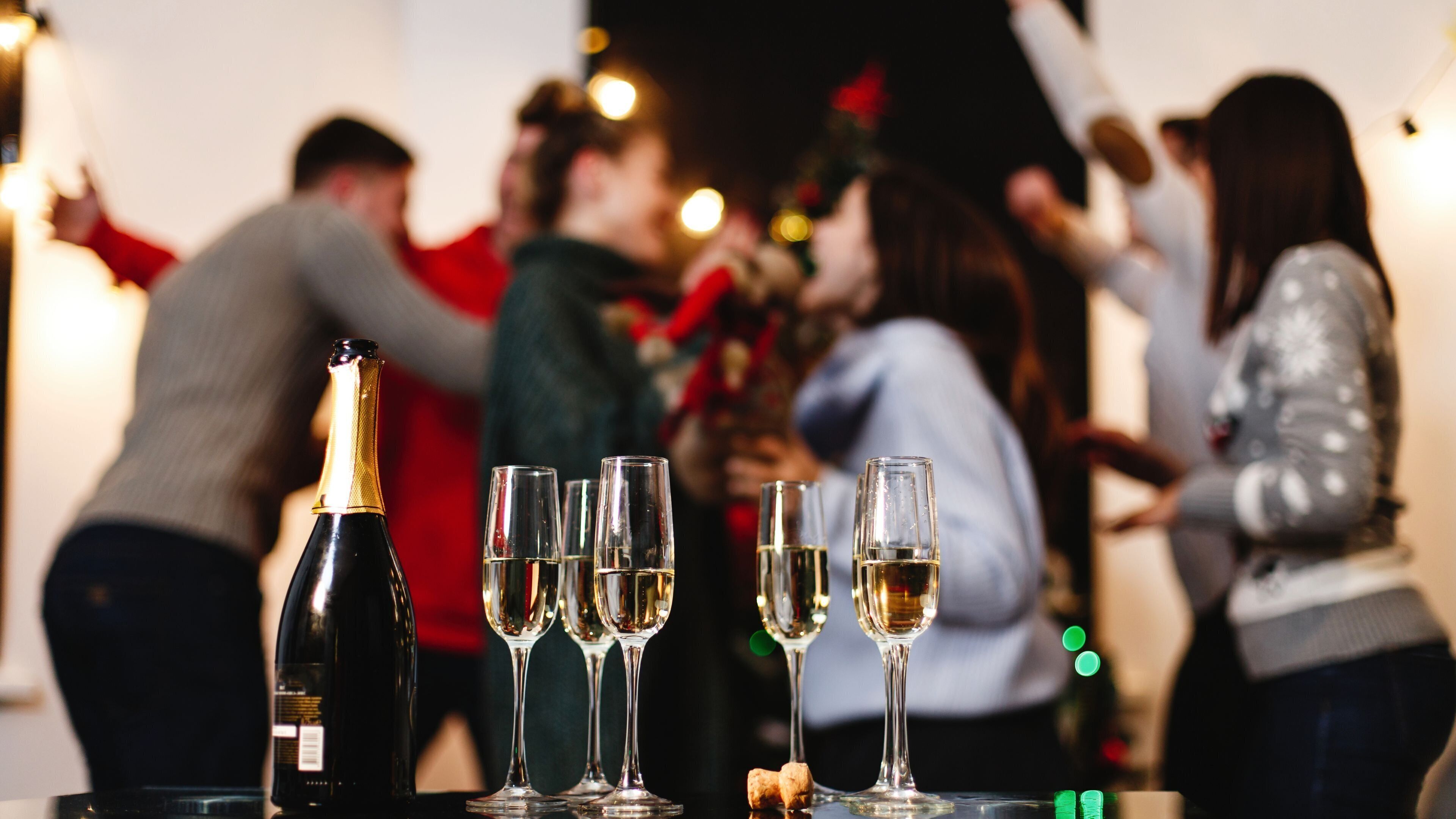 A bottle of champagne and several glasses on a table, with people in the background.