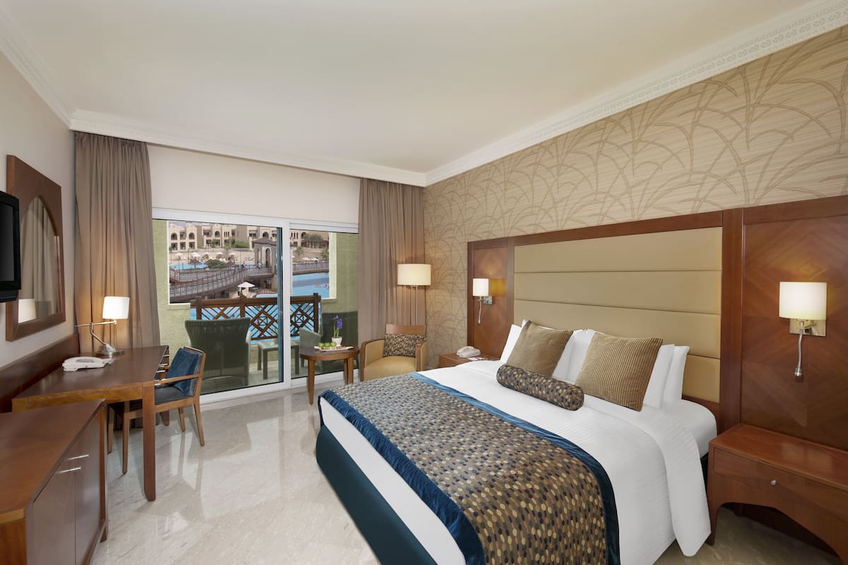 A hotel room with a large bed, a desk, a chair, and a view of the cityscape.