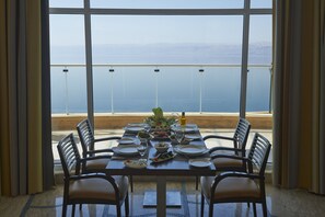 Mesa de comedor preparada para cuatro con vista al mar a través de grandes ventanales.