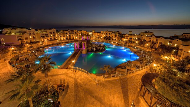 Un resort con varias piscinas, una fuente central y zonas ajardinadas a su alrededor.