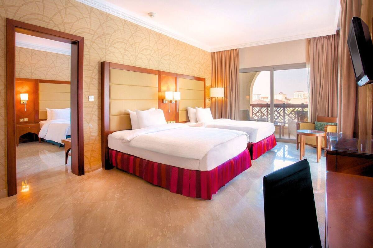 A hotel room with two beds, a TV, a balcony with a view, and a desk with a chair.