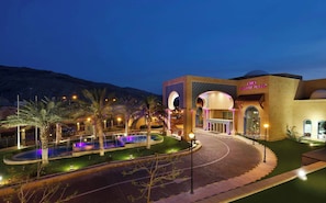 Ein Hotel mit Brunnen, Palmen und einem Bergpanorama.