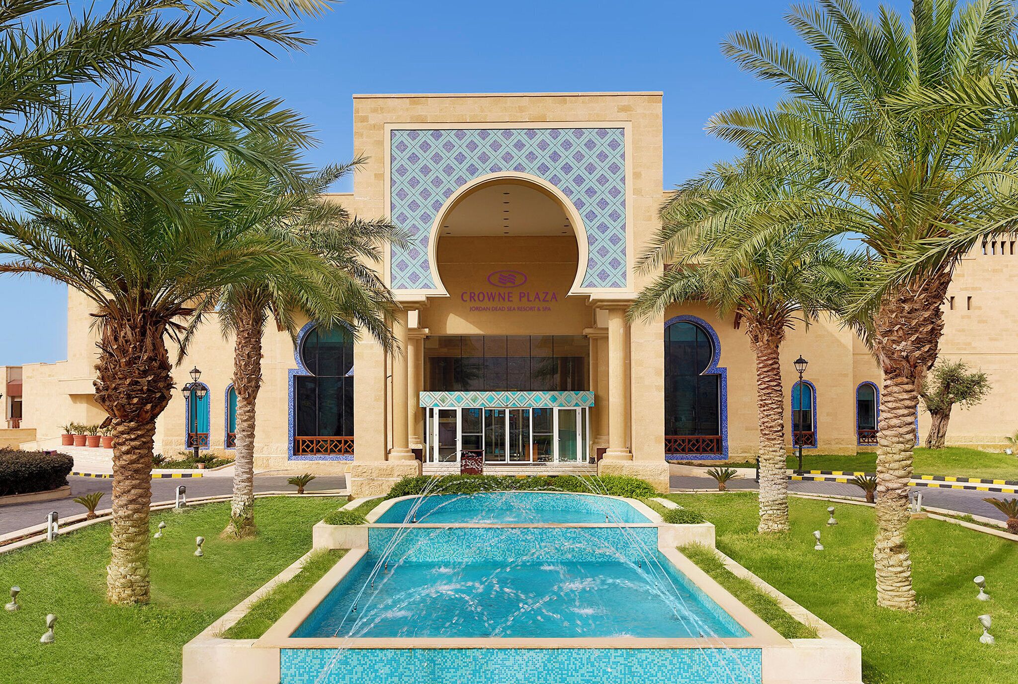 A building with a large arched entrance, palm trees, and a swimming pool.