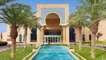 A building with a large arched entrance, palm trees, and a swimming pool.