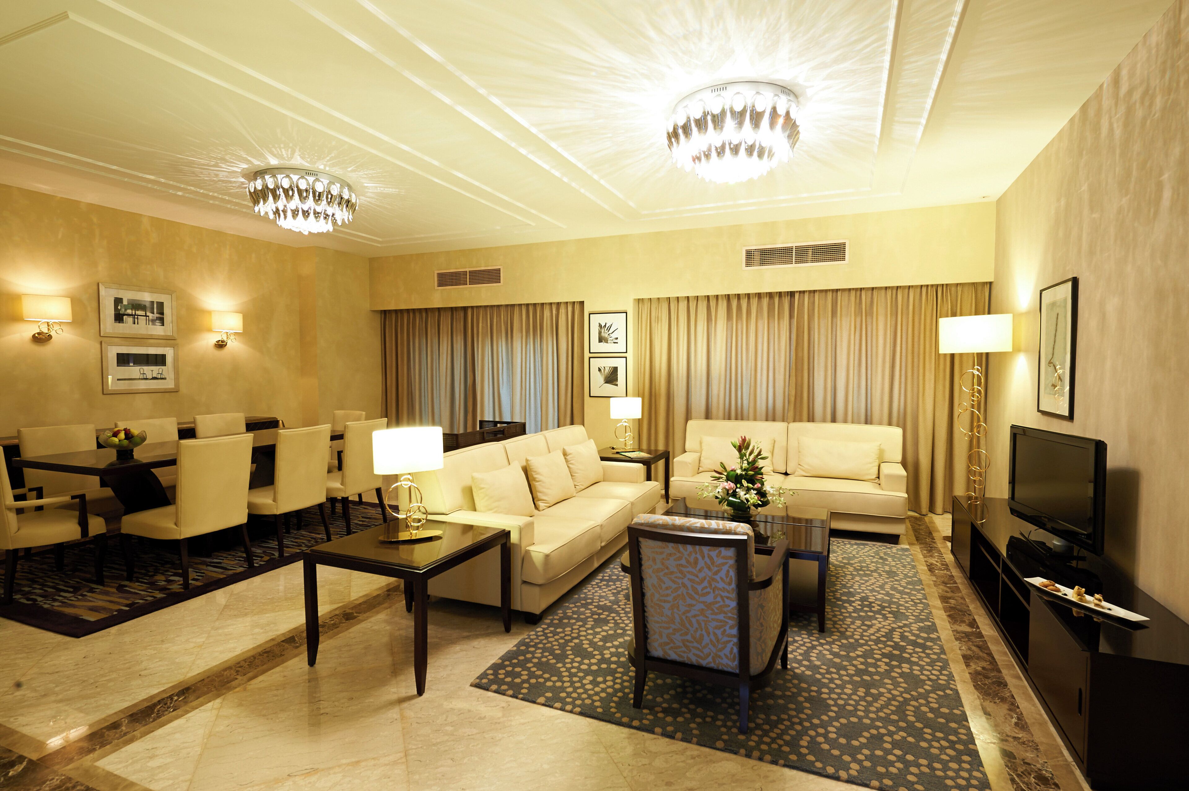 A hotel room with a living area featuring a sofa, a coffee table, a TV, and a dining set.
