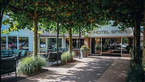 L’entrée d’un hôtel, avec un espace extérieur abrité aménagé en coin salon, des plantes en pot et un chemin dallé.