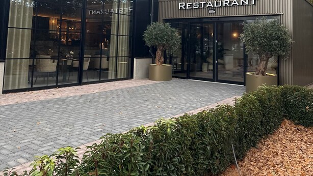 Un restaurant moderne avec une façade noire, de grandes fenêtres et des plantes en pot.