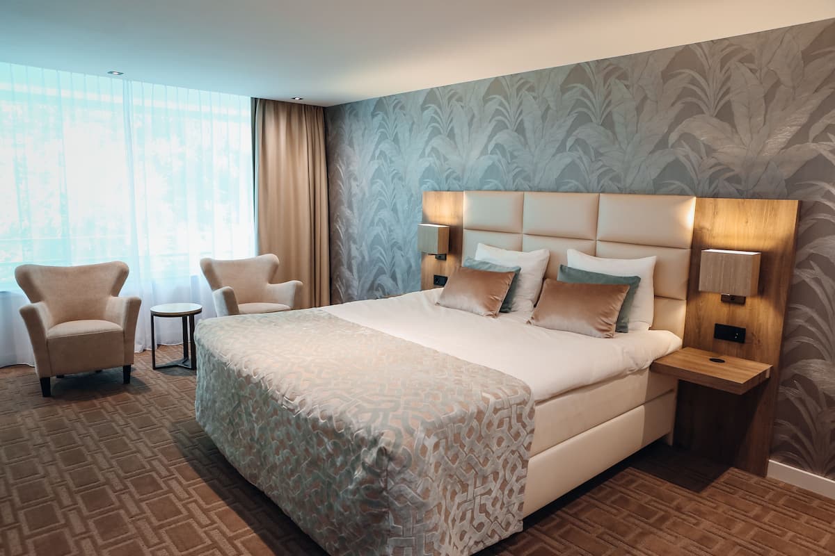 A hotel room with a large bed, two armchairs, a small round table, and a nightstand with lamps.