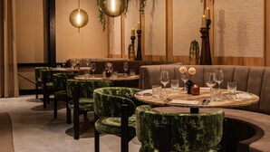 Un restaurant avec des tables rondes, des chaises recouvertes d’un tissu vert et des lampes suspendues.