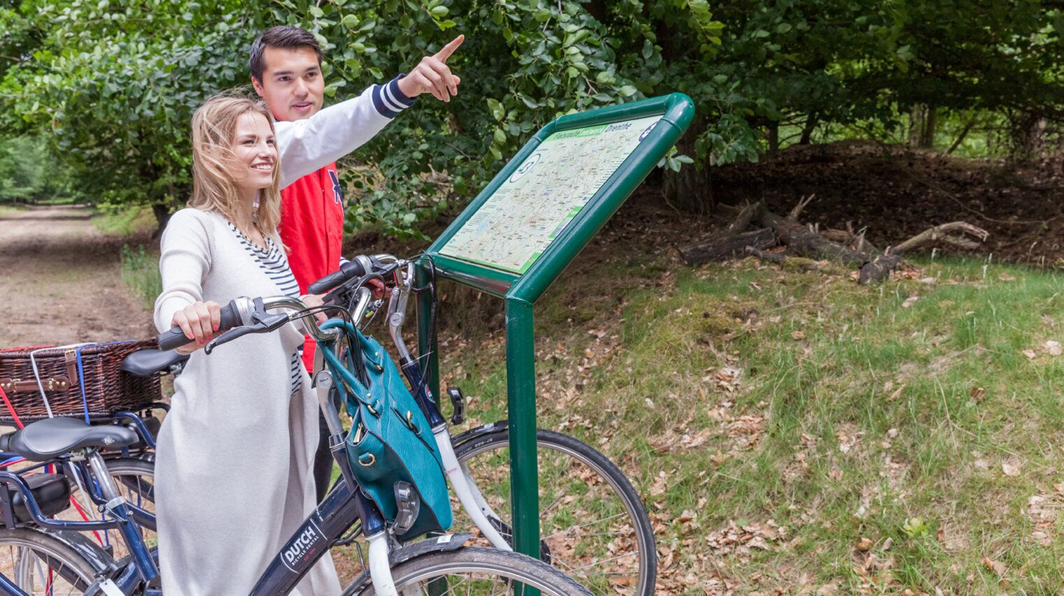 A map stand in a park with bicycles and a person pointing at it.
