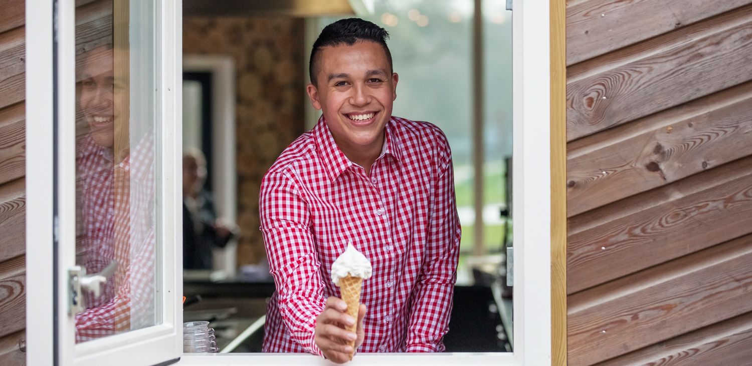 Una persona sosteniendo un cono de helado frente a una ventana de un edificio con revestimiento de madera.
