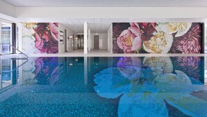 Une piscine intérieure moderne avec des murs recouverts de mosaïques et un fond en verre transparent.