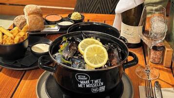Una mesa de comedor con una olla negra de mejillones, panecillos y una botella de vino.