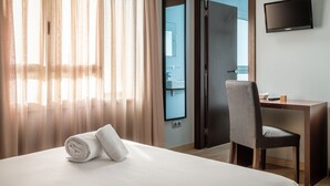 A hotel room with a bed, a desk, a chair, a TV, and a bathroom visible through an open door. - Hotel Madanis Liceo (L'Hospitalet de Llobregat)