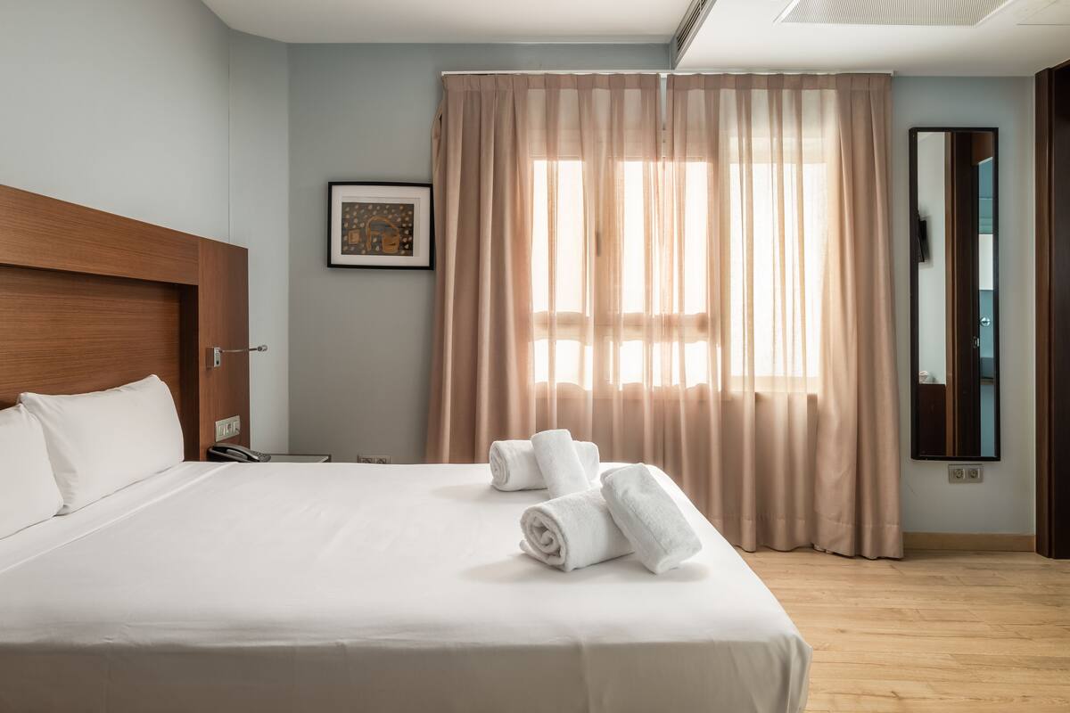Un lit bien fait, avec du linge de lit blanc, une tête de lit en bois et un téléphone sur la table de chevet.