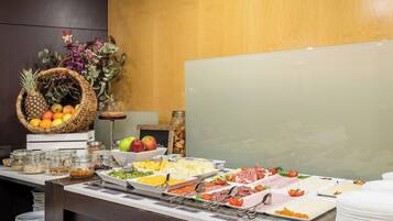 Ein reichhaltiges Buffet mit verschiedenen Speisen, darunter Obst, Käse und Fleisch, auf einer Theke vor einem Holzhintergrund.