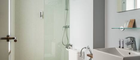 A modern bathroom with a glass shower enclosure, a white toilet, and a sink with a mirror above.