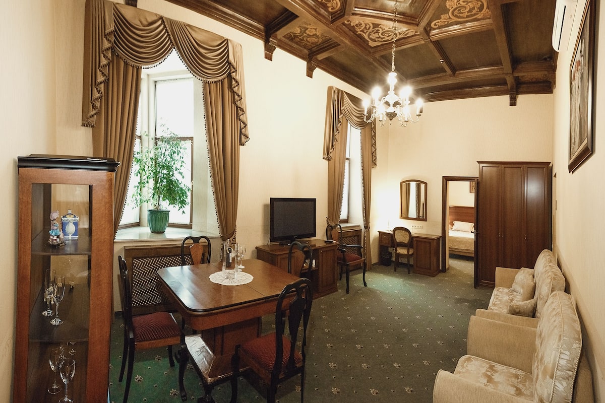 A room with a dining table, chairs, a television, a sofa, a bed, a mirror, and a chandelier.