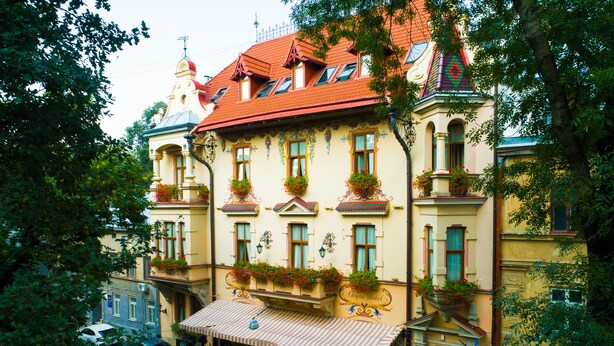 A multi-story hotel with a red-tiled roof, balconies with flower boxes, and a ground-floor café. - Chopin Hotel (Lviv)