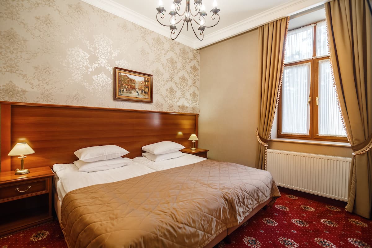 A hotel room with a large bed, wooden headboard, two bedside lamps, a framed picture on the wall, and a window with curtains.