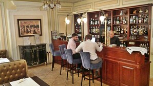 A bar area with wooden bar counter and stools, a chandelier, and a wall-mounted liquor display. - Chopin Hotel (Lviv)
