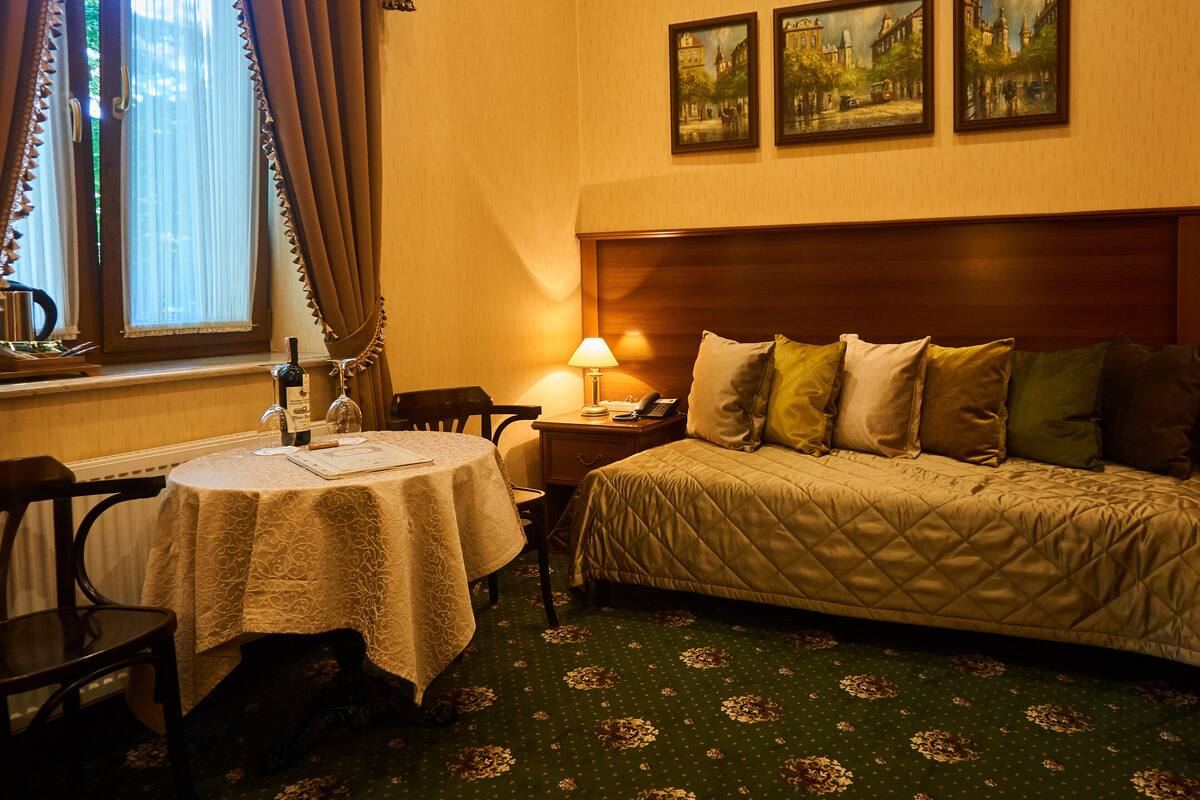 A hotel room with a bed, a table with a lamp, a chair, and a window with curtains.