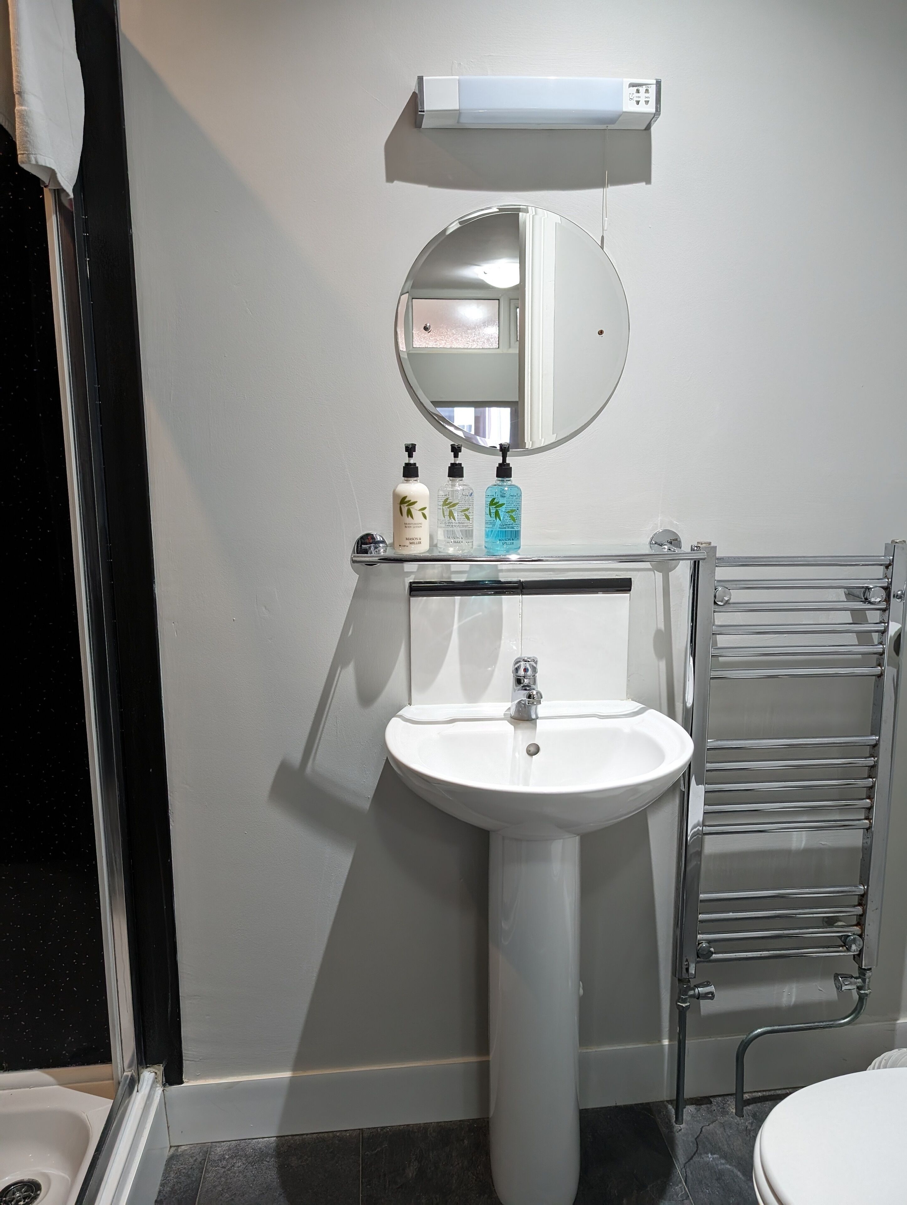 A bathroom with a white sink, a mirror, and a towel rack. There are three bottles of liquid soap on the sink.