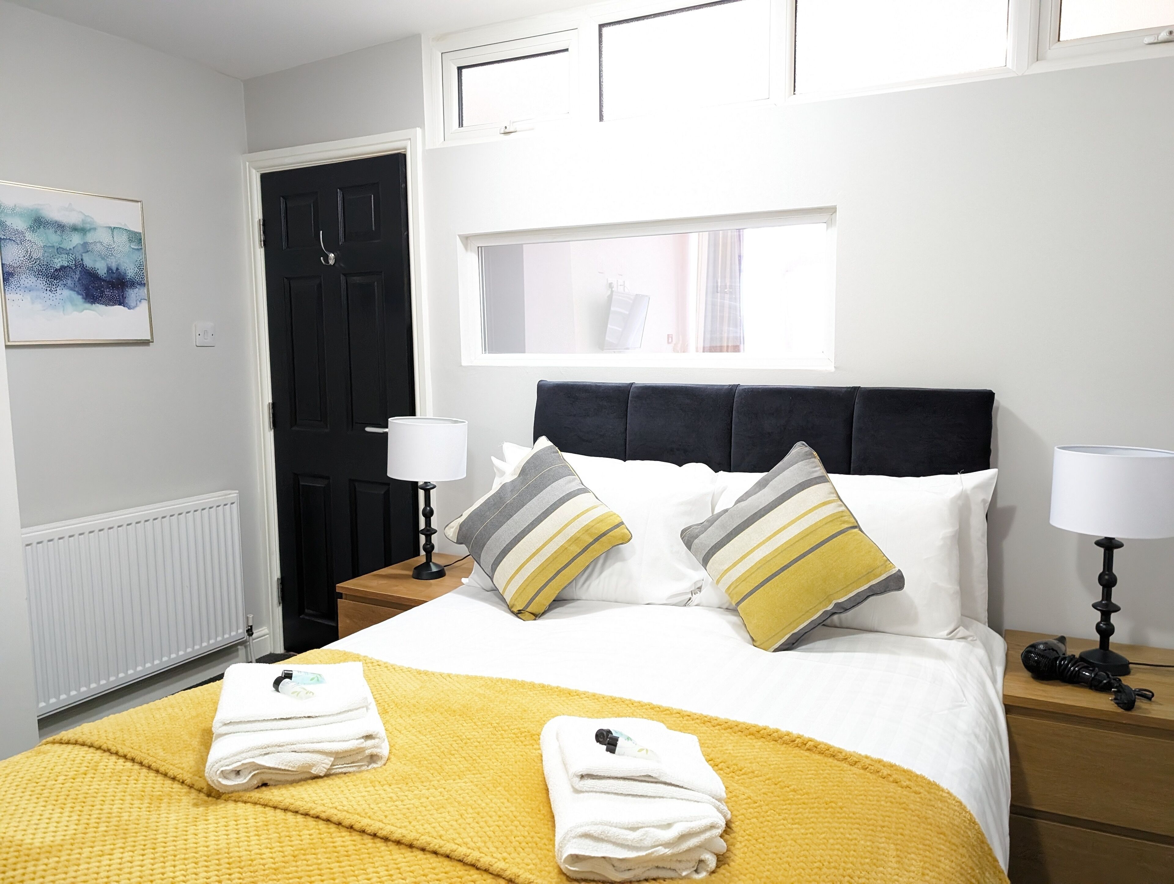 A neatly made bed with a yellow blanket, two pillows with stripes, and folded towels on the bed.