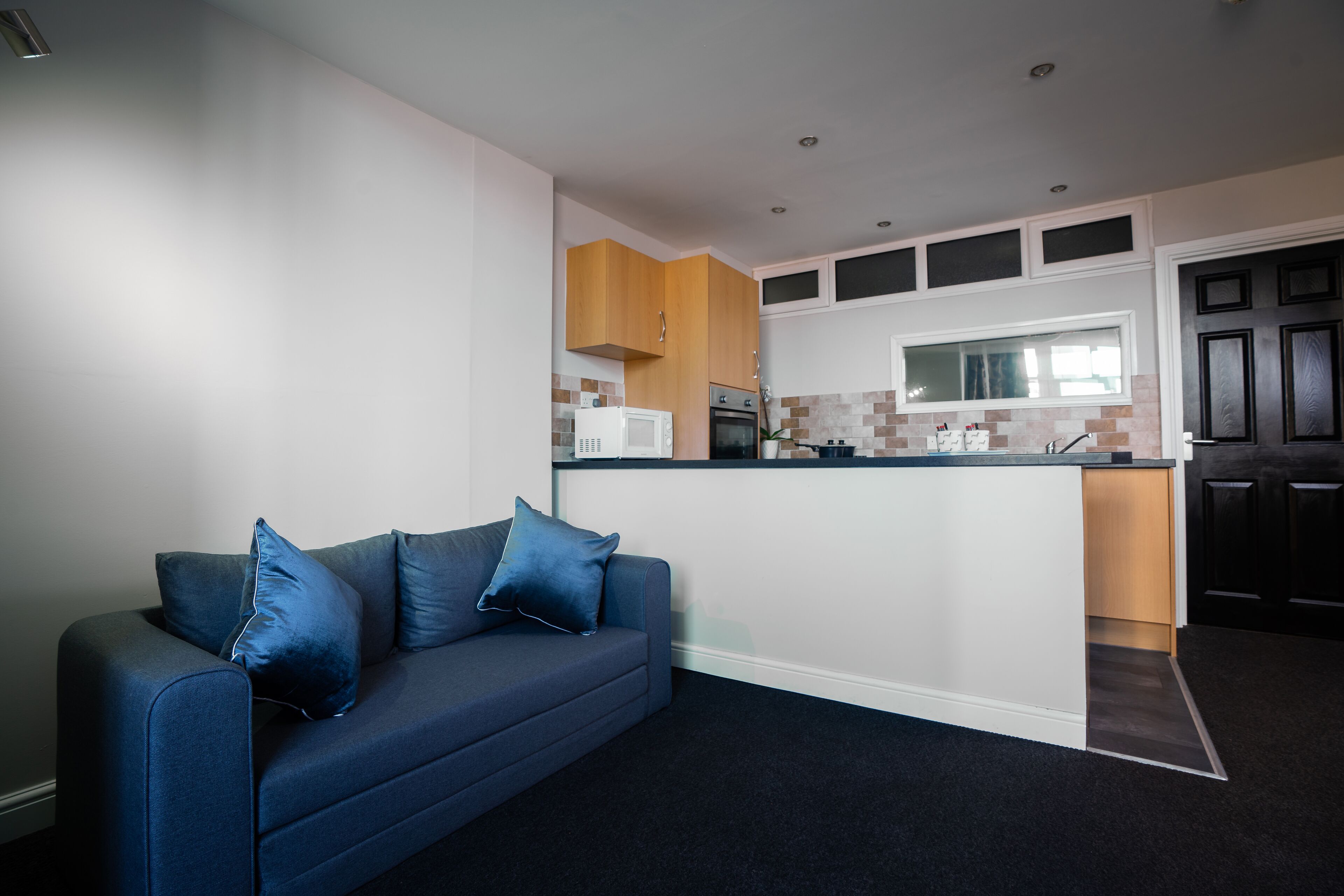 A modern kitchen with a built-in island, wooden cabinets, and a dark blue sofa with cushions.