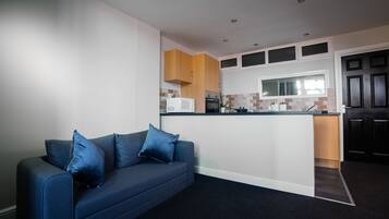 A modern kitchen with a built-in island, wooden cabinets, and a dark blue sofa with cushions.