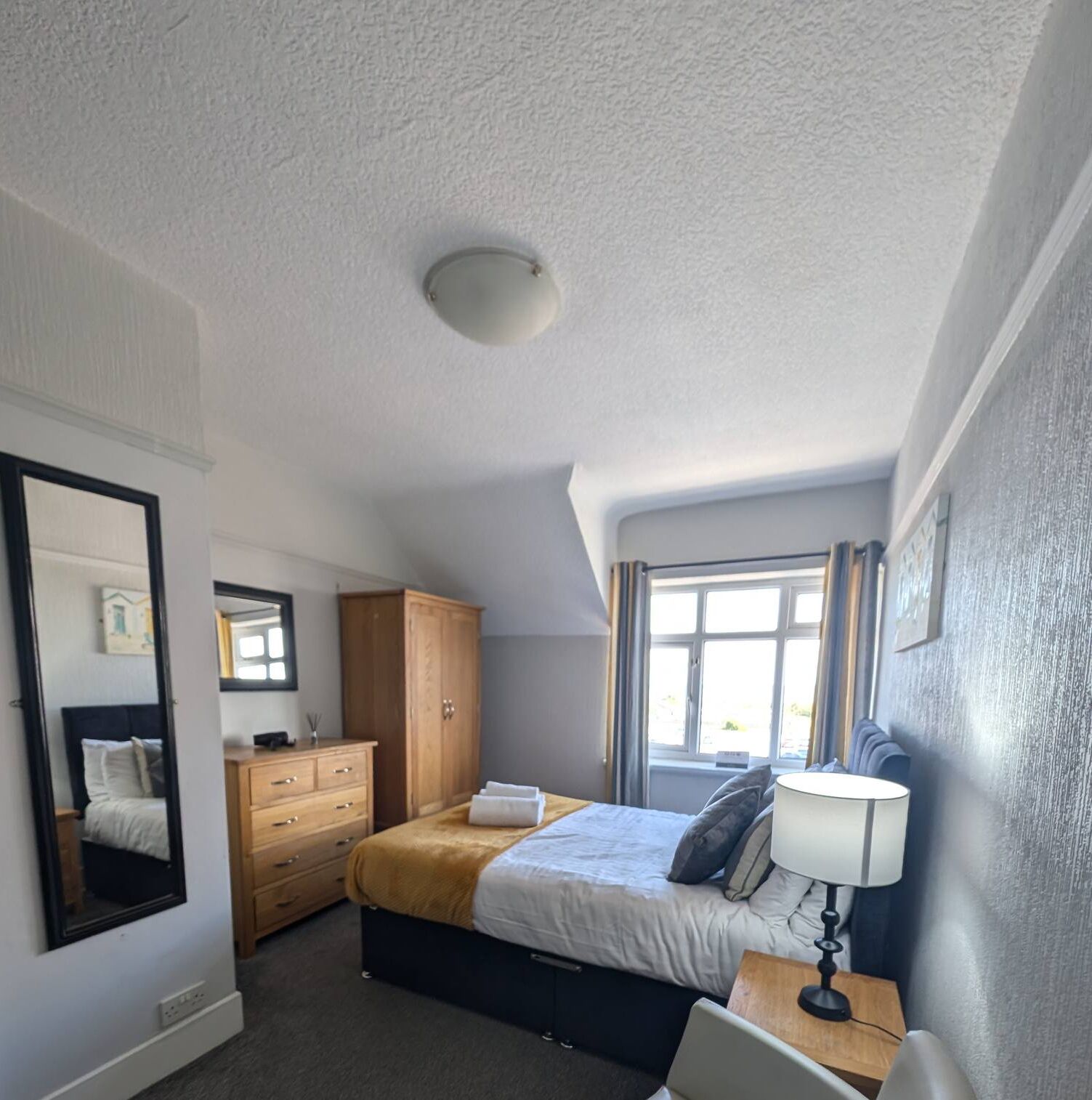 Un dormitorio con cama, cómoda, espejo y ventana.