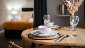 Una mesa de comedor dispuesta con platos blancos, fuentes, cubiertos y un florero con plantas secas.