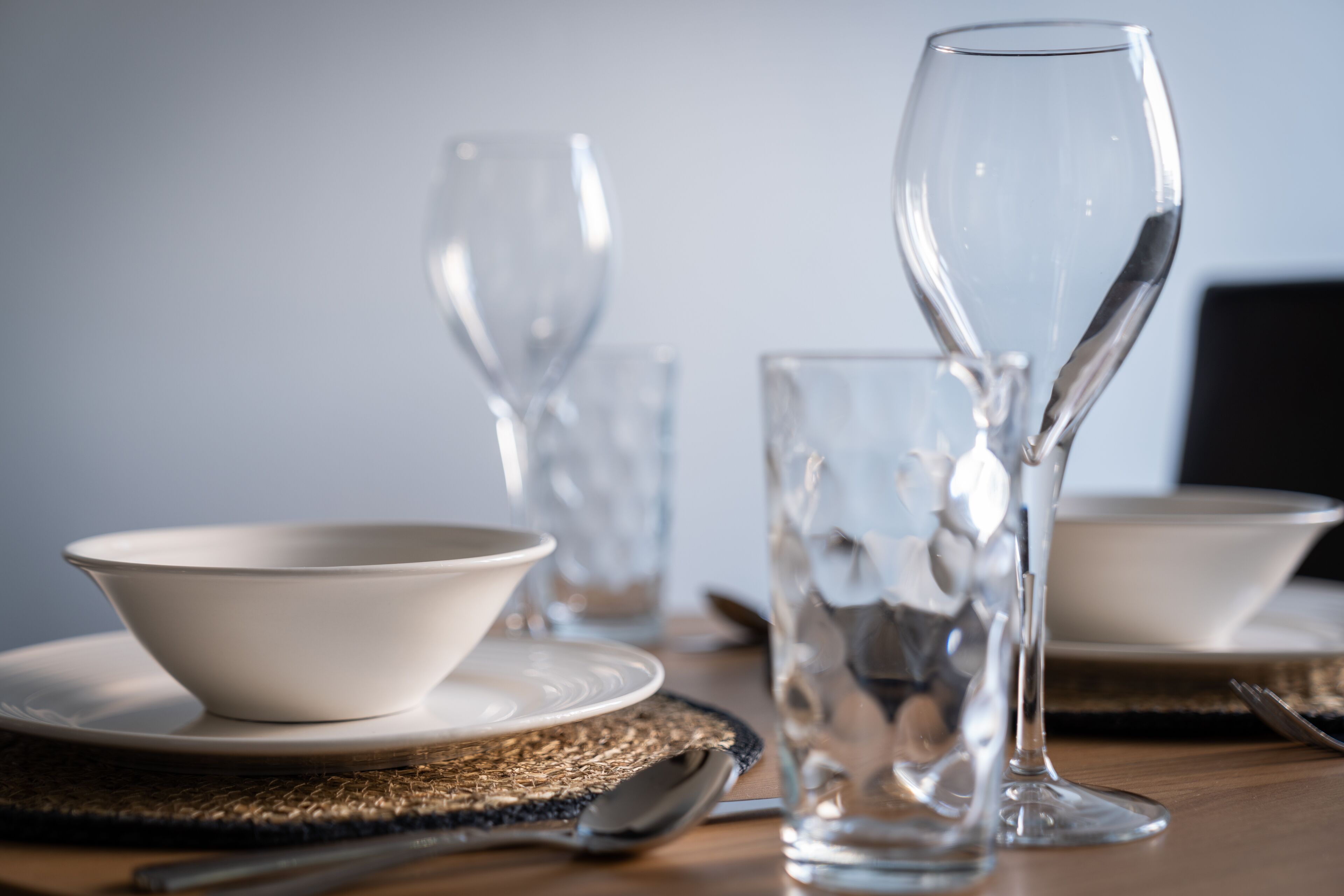Un tavolo da pranzo con bicchieri trasparenti, tra cui un bicchiere da vino e una ciotola, su un sottopiattino intrecciato.