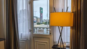 Quarto com porta que dá para área externa, luminária de pé e vista de um prédio com uma placa.