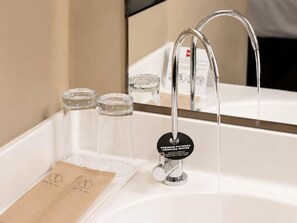 Un lavamanos de baño con un grifo moderno, dos recipientes de vidrio transparente y una tarjeta que dice 'PREMIUM FILTERED WATER'.