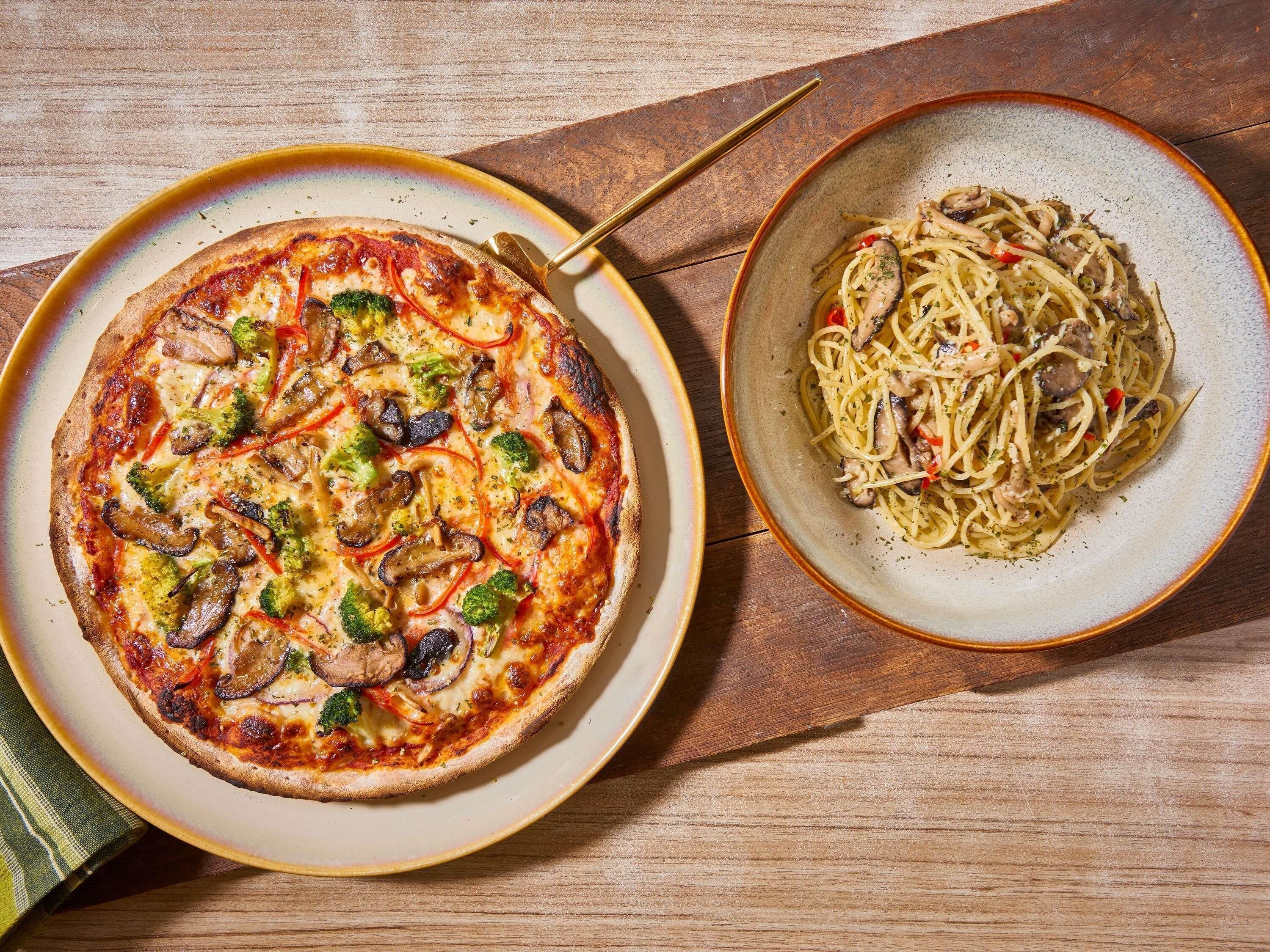 Um prato de pizza e massa sobre uma mesa de madeira.