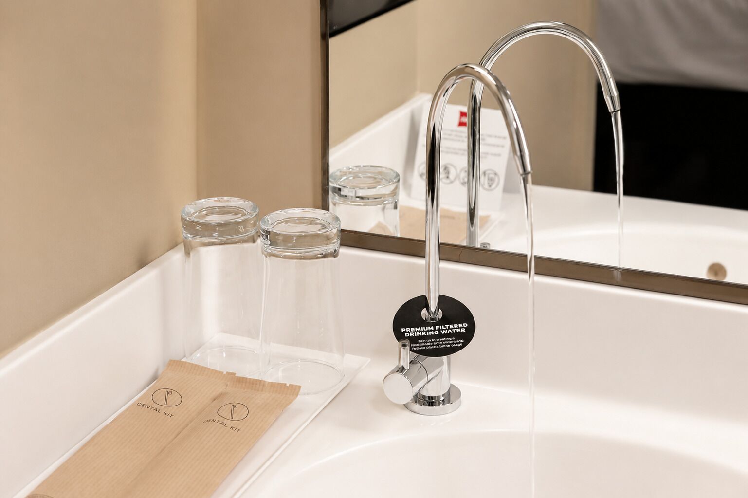 Ein Badezimmer mit einem modernen Wasserhahn, einem Spiegel und drei klaren Glasbehältern auf einer Holztablett.