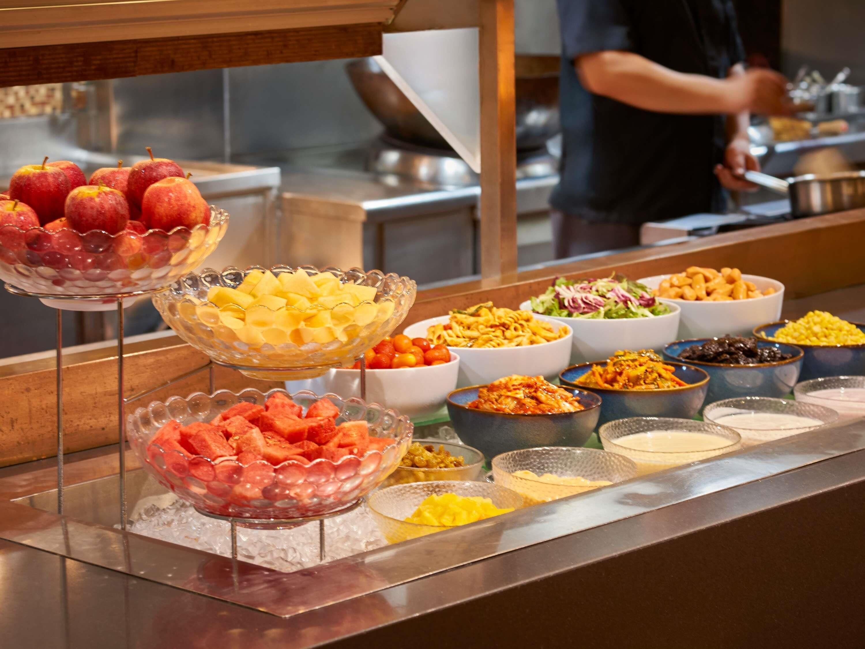 Un bufé con diversas opciones de comida, incluyendo frutas, ensaladas, pasta y otros platos.