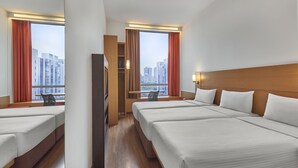 Habitación de hotel con dos camas, cabecero de madera, ventana con cortinas y vistas a edificios.