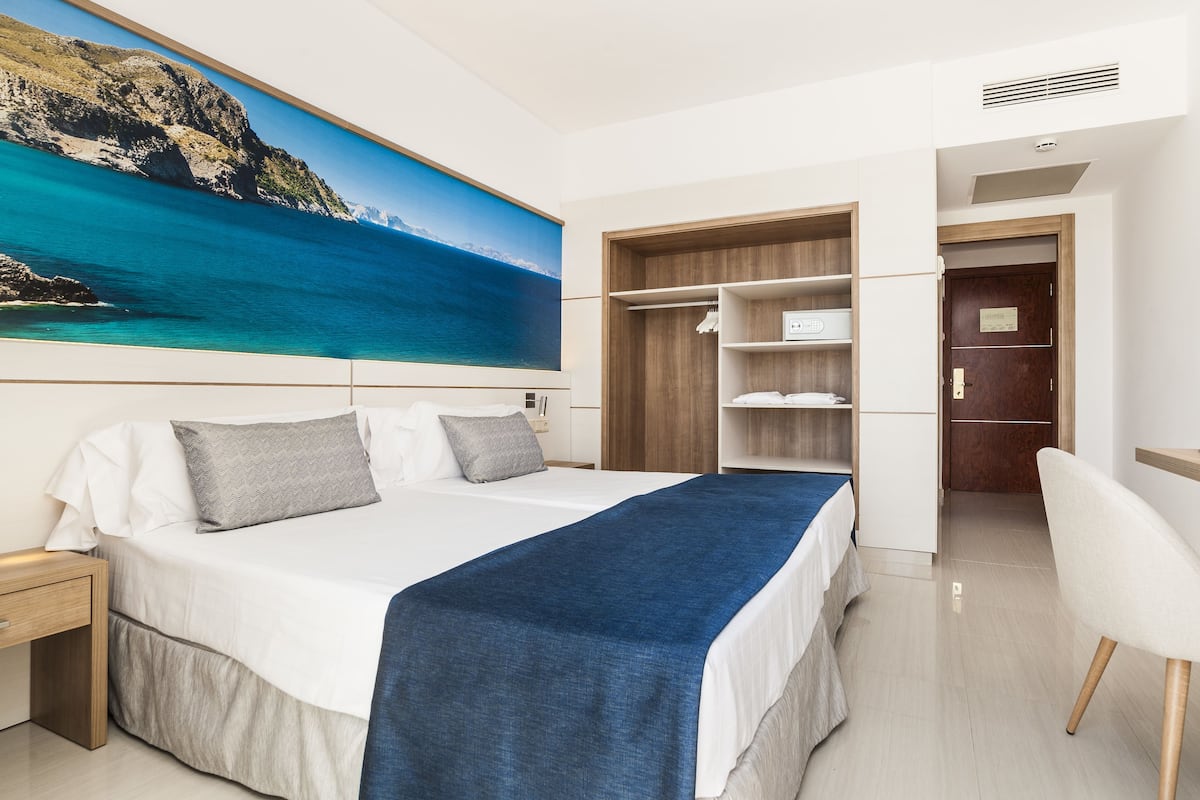 A modern hotel room with a bed, a desk, and a wardrobe.