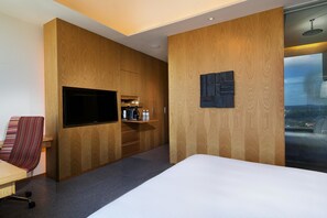 Une chambre d’hôtel moderne dotée d’un grand lit, d’un téléviseur fixé au mur, de panneaux décoratifs en bois, d’un petit coin salon et offrant une vue sur l’extérieur.