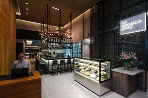 Un espace bar moderne avec un présentoir de desserts, un chef en pleine préparation et une pancarte indiquant : « le garde-manger des confitures ».