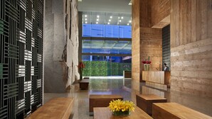 Un vestíbulo moderno con bancos de madera, una pared de vidrio y vistas al exterior con vegetación.